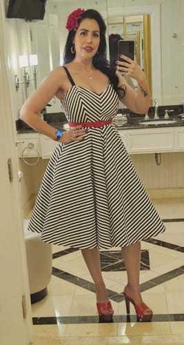 Reviewer taking a mirror selfie in the black and white striped Dollface Dress, styled with a slim red belt.