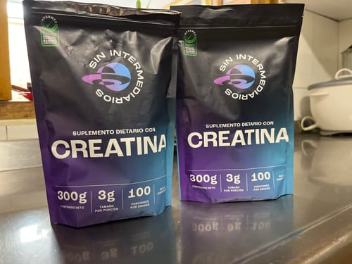 Reseñador muestra dos empaques negros de Creatina Monohidrato sobre la encimera de una cocina.