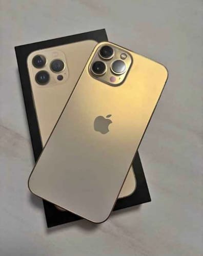 Un cliente muestra la parte trasera de su iPhone 13 Pro dorado, colocado sobre su caja negra.