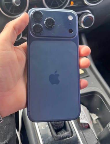 Un cliente sostiene la parte trasera de un IPHONE 17 PRO MAX azul oscuro dentro de un coche.