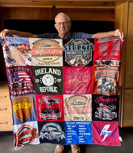 Customer holding up a colorful Premium T Shirt Quilt made from a collection of Sturgis motorcycle rally t-shirts.