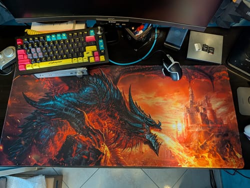 Customer's large Liquid Black desk mat with a colorful dragon fanart on a desk with a keyboard and mouse.