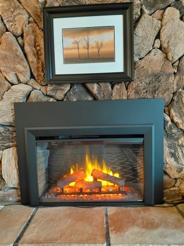 Customer's SimpliFire Electric Fireplace Insert with glowing flames, installed inside a large stone fireplace.