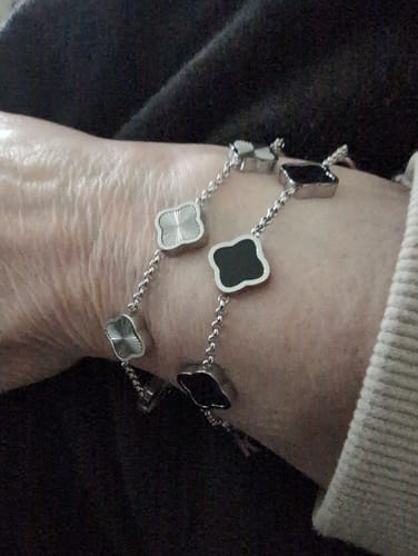 Customer's wrist wearing two Celine Silver Clover Bracelets, one with textured silver and one with black enamel clovers.