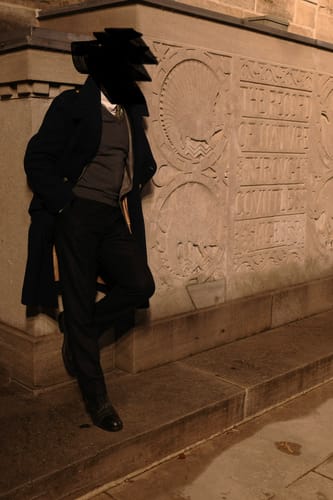 Reviewer wearing the dark 1940s British Royal Air Force Greatcoat layered over a sweater, leaning against a stone wall at night.