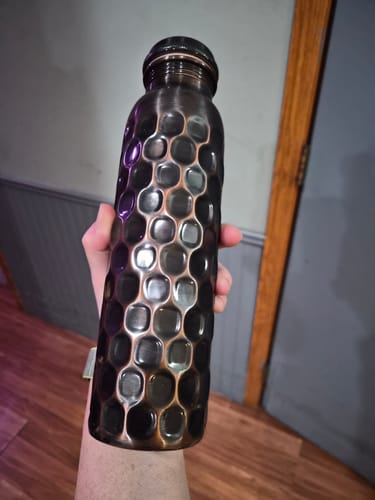 Customer holding their antique black copper water bottle, showing its unique diamond-cut texture.