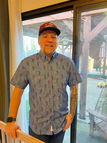 Customer smiling while wearing the blue Spider-Man 'The Meme' Short Sleeve Shirt indoors, showing the fit and pattern.