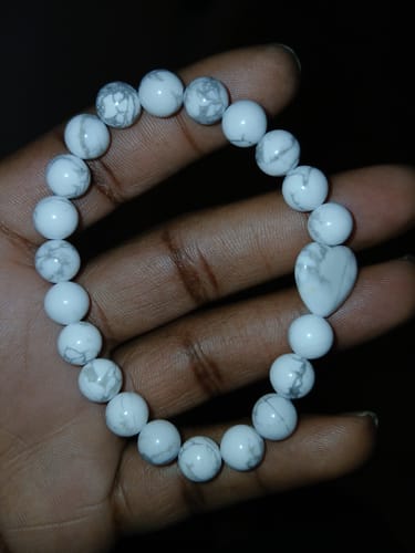 Reviewer's hand holding a white, marbled bead bracelet from the VIP Crystal Club with a heart-shaped bead.