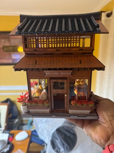 Reviewer holding an unfinished 3D puzzle, a wooden miniature of a two-story bakery.