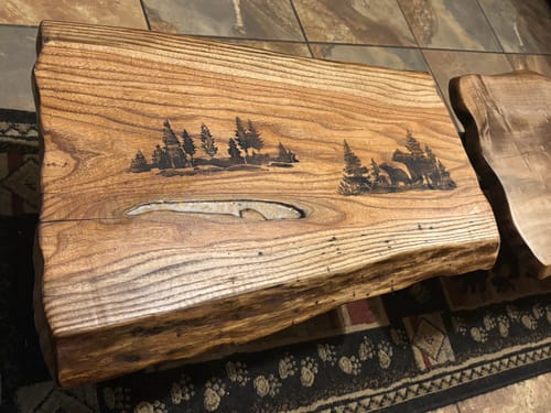 Customer's live-edge wood slab with a crisp, wood-burned Adirondack scene, a result of the Wood Pre-Treatment.