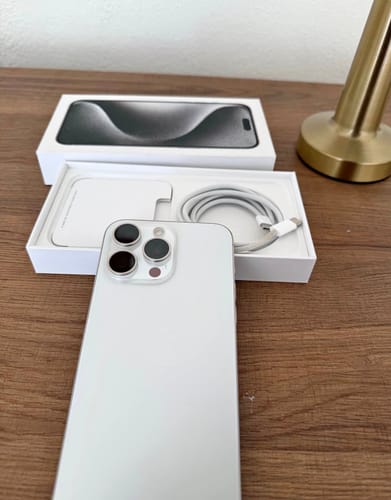 El cliente muestra un iPhone 15 Pro Max blanco, nuevo y fuera de su caja con sus accesorios.