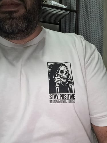 Reviewer wearing the white Mystery Tee with a black skeleton graphic that reads 'STAY POSITIVE'.