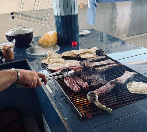 Cliente asando tiras de Asado de Tira en una parrilla junto con tortillas y cebollas.