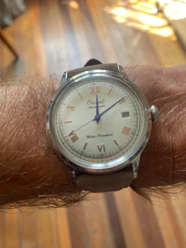 Un cliente mostrando su reloj Orient Bambino en la muñeca, con una esfera clara y elegantes agujas azules.