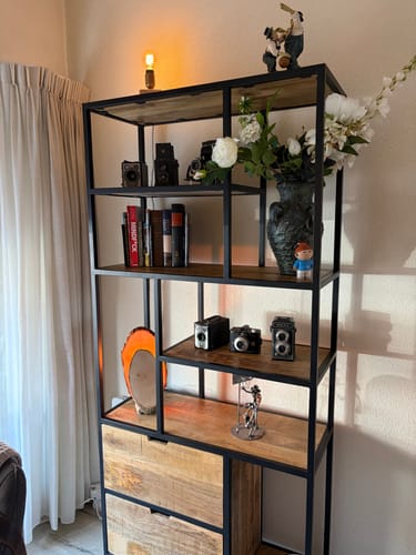 Recensent toont de metalen boekenkast met 2 lades, gestyled in een woonkamer met decoraties.