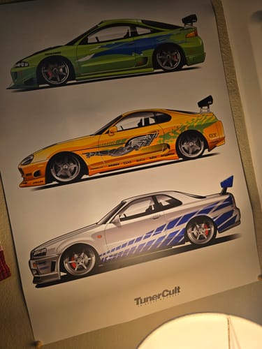Reviewer's 'Fast Rides' poster showing detailed illustrations of three colorful tuner cars hanging on a wall.