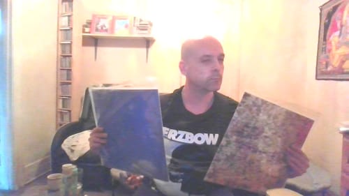 Reviewer sitting indoors holding up two of their Custom Vinyl Records with different artistic covers.
