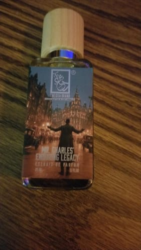 A customer's bottle of Mr. Charles' Enduring Legacy fragrance with a wooden cap, placed on a dark wood surface.