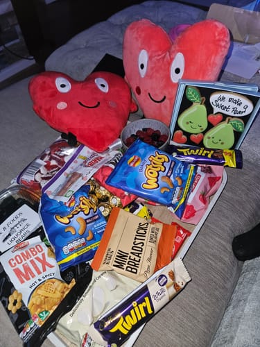 Customer's 'We Make A Sweet Pear' Biscuit Box seen open amongst a large collection of snacks and heart-shaped plush toys.