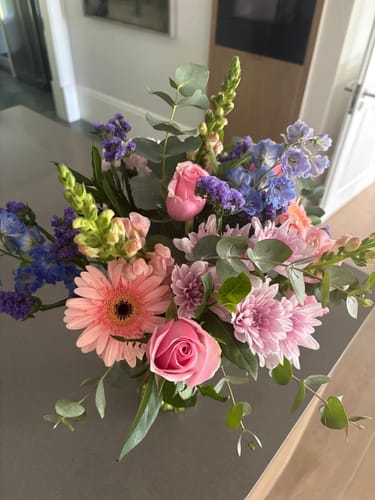 Customer's 'Glee in a Jar' bouquet showing vibrant pink and purple flowers on a dark countertop.