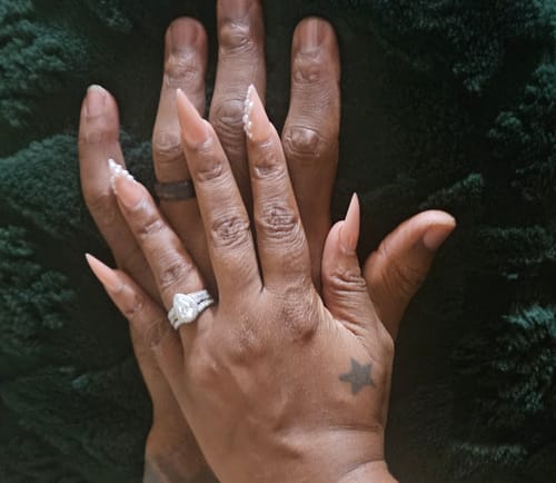 A customer's hand wearing a dark band, held together with their partner's hand on a green plush surface.