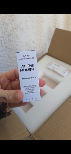 Kunde hält die weiße Schachtel des ätherischen Öls At The Moment in der Hand.