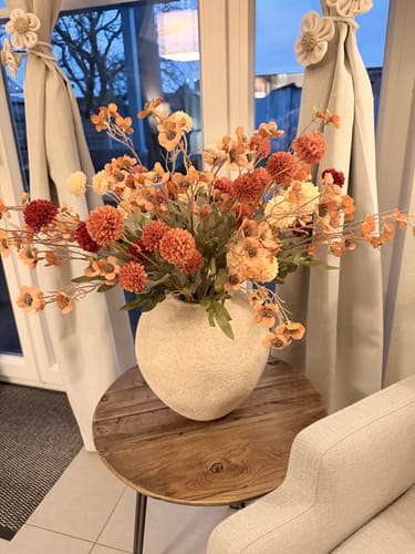 Recensent toont de beige Arda vaas, gevuld met een groot boeket oranje bloemen op een houten bijzettafeltje.