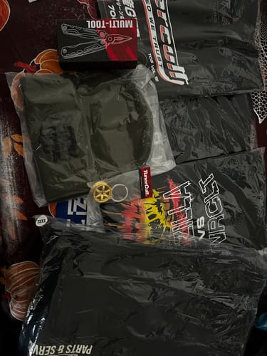 Customer displays the contents of their CULTIMATE MYSTERY CASH BOX, including packaged shirts, a multi-tool, and other accessories.