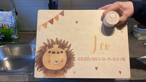 Ein Kunde hält den personalisierten Deckel der hölzernen Erinnerungsbox mit Löwen-Motiv.