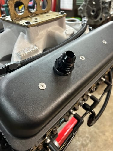 Customer's close-up of the black SBC 12AN Valve Cover Adapter Fitting installed on a textured engine cover.