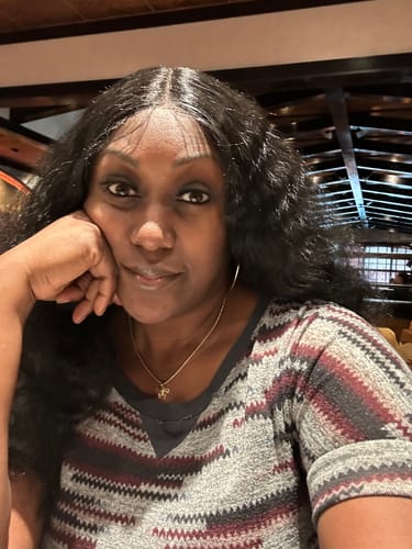 Close-up of a reviewer wearing the Sensationnel Dashly wig, styled with a center part and full, puffy black hair.