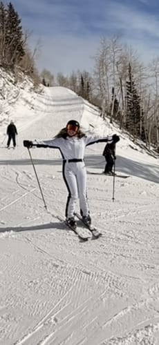 Reviewer skiing on a snowy slope in the white and black one-piece ski suit with arms outstretched.