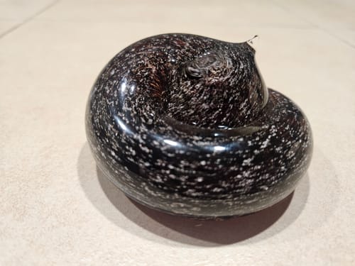 Reviewer's dark, speckled glass Sleeping Cat memorial with infused ashes, shown on a tiled surface.