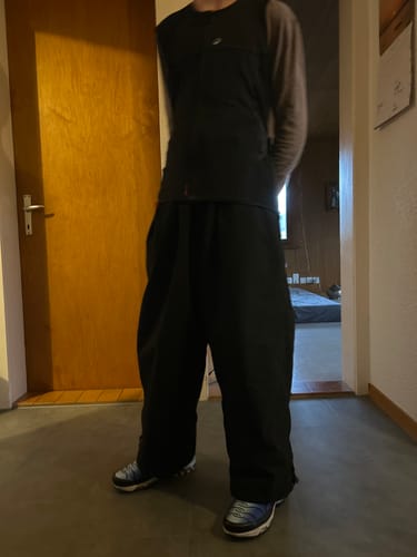Reviewer standing indoors to show the very baggy fit of the black snow pants.