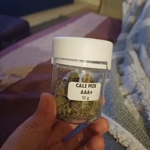 Customer holding a small, clear jar containing 10g of CALI MIX AAA+ flower, showing the buds inside.