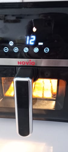 Prim-plan de la un client cu friteuza Novio StonePro în funcțiune, cu afișajul tactil iluminat și setat la 12 minute.