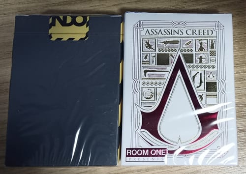 Customer's two sealed Mystery Decks. One is dark blue and the other is a white and red Assassin's Creed themed deck.