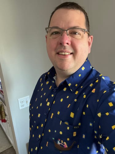 Reviewer smiling while wearing the navy Disney's Tangled "Lanterns" shirt, showing the pocket graphic.