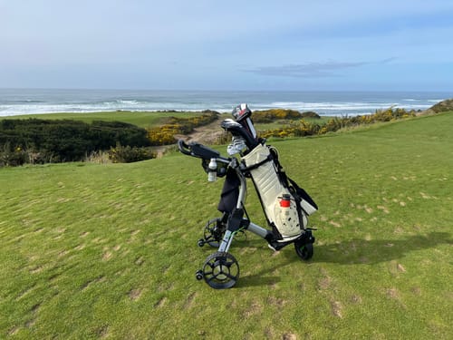Customer's Cybercart with a golf bag, pictured on a hilly coastal golf course with the ocean in the background.
