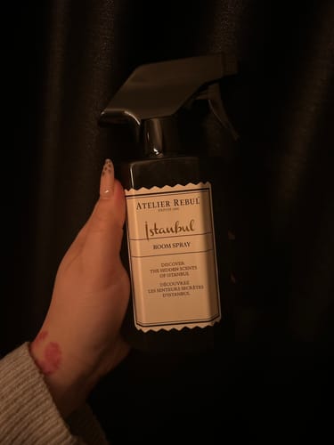 Recensent houdt de donkere fles Istanbul Room Spray vast tegen een zwarte achtergrond.