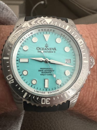 Close-up of a customer's Oceaneva Damascus steel watch with a sky blue dial, worn on their wrist.