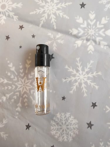 Reviewer's small sample vial of Honeyberry perfume on a grey background with white snowflakes and stars.