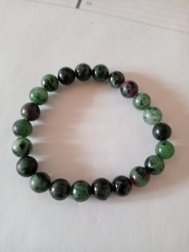 Un client montre son Bracelet Rubis Zoïsite, avec des perles vertes et rubis, posé à plat sur une surface.