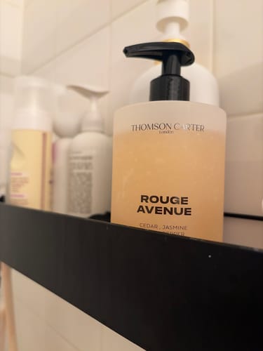 Reviewer's Rouge Avenue Body Wash in a frosted bottle on a black bathroom shelf.