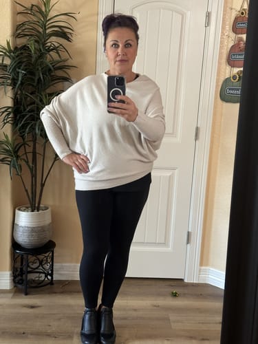 Reviewer taking a mirror selfie wearing the off-white Asymmetric Draped sweater with black leggings.