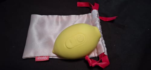 Customer's yellow Lem Clitoral Massager resting on its light pink satin pouch with a red drawstring.