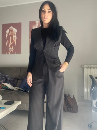 Recensore indossa il Tailleur Smanicato nero. Il completo a righe ha un gilet aderente e pantaloni a gamba larga.
