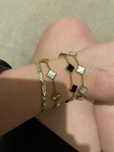 Customer's wrist showing two stacked Celine Clover Bracelets, one with white mother of pearl and one with black enamel clovers.