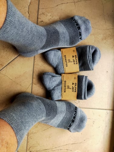 Customer wearing a pair of grey Quarter Socks, with two new pairs in their packaging on the floor.