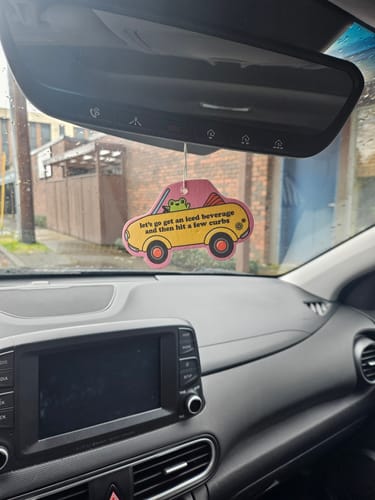 Customer's yellow, car-shaped air freshener with a frog driving, hanging from a car's rearview mirror.